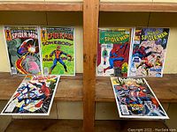 Photo showing the front covers of six vintage Spider-Man comics arranged on a wood shelf, including Peter Parker The Spectacular Spider-Man, Web of Spider-Man, and Spider-Woman issues.