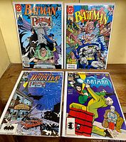 Four Batman comic books laid out including Detective Comics and Batman series, show front covers with colorful illustrated comic art.