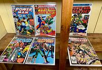 Six different issues displayed together showing full covers of each comic comic book issue, held in protective sleeves on wooden surface.