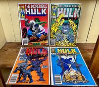 Full view of all four Hulk comics standing on a wooden surface against a white wall. Shows comic covers and size relation.