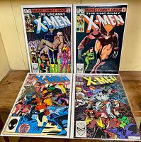 Four Uncanny X-Men comic issues (#167, #173, #193, #235) arranged on a wooden surface with visible cover art showing various X-Men characters and colorful graphics.