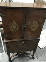 Front view of the antique wooden radio cabinet showing painted floral details, iron hinges, and carved drawer front.