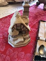 David Winter "Audrey's Tea Room" cottage figurine with detailed thatched roof and cobblestone path, displayed on red patterned cloth.