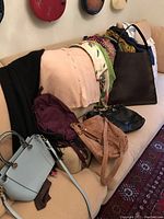 Photo showing handbags, scarves, and wraps arranged on a beige couch, handbags in front, scarves and wraps draped behind.