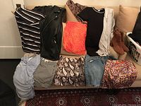 Assorted women's clothing and cognac suede boots arranged on sofa and floor with various patterns and colors visible.