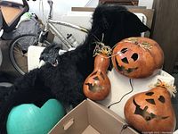 Photo of three large wooden gourds carved with jack-o'-lantern faces and a large black bat decoration with fur texture, showing the set of Halloween decorations.