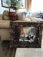 Photo showing the carved Chinese wedding basket beside a sofa and the oil painting in a carved wooden frame leaning against the sofa on the floor.