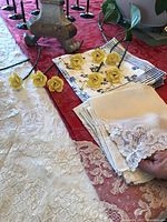 Yellow porcelain stem roses alongside folded lace napkins and plain napkins on a red tablecloth with lace overlays.