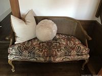 Full view of the settee showing wooden frame, cane backrest, floral seat cushion, and small pillows included.