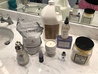 Overview of all items on marble counter including shampoo jug, bath soak, spray bottles, candle, perfume, and bath salts jar