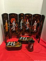 Photo showing six-panel black lacquered tabletop folding screen with painted Asian traditional figures and scenic elements, front view.