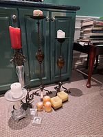 Three metal decorative candlestick holders, tallest at 30 inches, displayed with a variety of pillar and votive candles on and around them