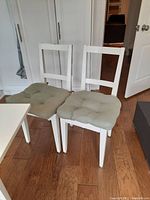 Pair of white wooden chairs with light green tufted cushions on a wooden floor.
