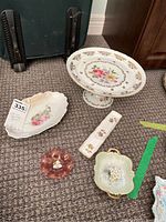 Full view of all items in the lot including cake stand, small serving dishes, and glass trinket holder on carpet.