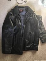 Full view of the black leather jacket with removable lining visible, laid flat to show front and open jacket collar area.