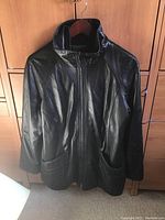 Front view of black leather jacket on hanger showing zipper, pockets and collar