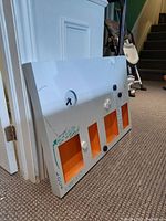 Side angle view of white magnetic board with orange cubbyholes and round magnets attached. The built-in clock is visible on top left. The board has handwritten notes and some scuff marks.