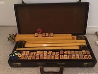 Opened black rectangular vintage case showing mahjong tiles at bottom and wooden racks on top with score counters.
