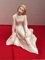 Front view of Royal Doulton Across the Miles porcelain figurine showing seated woman in white dress with detailed elongated gown and hands resting gently on knees.