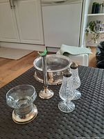Photo showing silver plated serving dish, bud vase, salt and pepper shakers and glass bowl with silver plate base on a black surface with kitchen background.