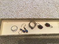 Photo showing two rings and two pairs of earrings arranged in a tray on carpet.