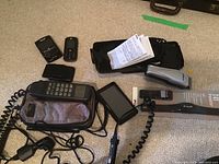 Lot displayed on carpet showing all items: Tandy car phone in carrying case, Conair hair clipper, Garmin GPS, Polar T41, Blackberry and Motorola phones, and small black case with papers.