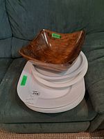 Wooden bowl stacked on top of white plastic trays and plates on a green couch.