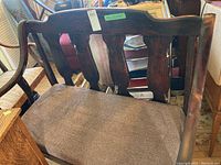 Front view of antique solid wood bench showing curved wood backrest and brown upholstered seat cushion.