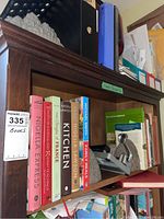 Cookbooks and hardcover books on a dark wood shelf with a metal hole punch and stone bookends