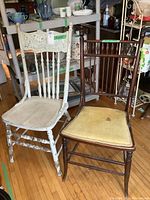 Photo showing two vintage wooden chairs side by side, the white painted chair on the left with visible wear and chipping, and the dark stained chair on the right with yellow upholstered seat with some stains.