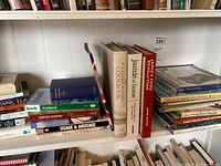 Middle shelf of bookcase showing a variety of books including cookbooks like 'Jamie's Food Revolution', 'The Food Cookbook', travel guides like 'Iceland' by Bradt, crafting books like 'Great Barrier Stamping', and 'Simple Textile Printing and Dyeing Techniques'