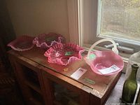 Four pink glass pieces: three ruffled edge bowls and one basket displayed on a wooden surface