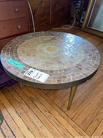 Round mosaic tile side table with a 22-inch diameter top and metal legs positioned on a wooden floor.