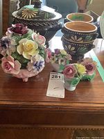 Overview photo of six porcelain flower arrangements with different sizes and colors, showing chips and broken stem.