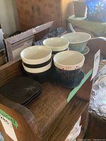 Photo showing four black sake cups with white rims and botanical pattern, four matching square black saucers, one larger decorative small rice bowl with colorful floral designs.