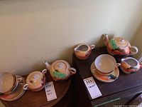 Full view of tea set pieces arranged showing teapots, cups, saucers, creamers, and sugar bowl with labels and scenic Japanese design.