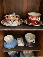Display of four teacup and saucer sets on wooden shelves, showing color and design variations