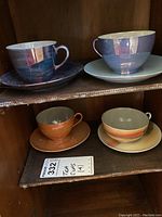 Four vintage teacups and saucers arranged in a wooden cabinet, showing color and condition.