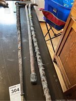 Three vintage walking canes laid flat on a table; one wrapped in leather, one natural wood stick with rubber tip, and one textured wood cane.