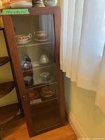 Front and angled view of solid wood cabinet with glass door showing shelves and interior contents.
