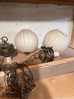 Photo showing two antique hanging light fixtures with round opaque white ribbed glass globes and metal fittings with chains.