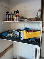 Shelf with various automotive supplies including battery charger, spray bottles, tools, and accessory case.