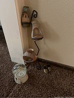 Photo of a black metal decorative stand holding three lanterns, a large clear snow globe with a white base, and a pair of small shiny figurines that look like shoes placed on the carpet.
