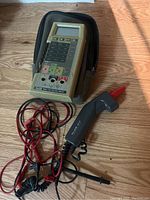 Fluke digital multimeter with attached temperature probe and measurement leads on wooden surface with protective case.