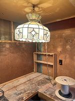 Photo of stained glass hanging lamp suspended by chain above a workbench, showing lamp detail and surrounding pegboard walls.