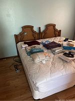 King size wooden headboard against wall with mattress on box spring and items placed on mattress.