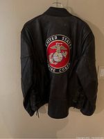 Back view of the black leather motorcycle jacket with large United States Marine Corps emblem embroidered in red, gold, and white on the back.