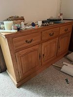Oak buffet cabinet viewed from the side showing overall shape, wood grain, and metal handles with items on top.