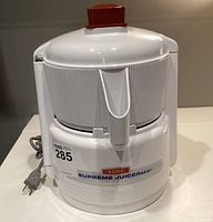 Front view of white Acme Supreme Juicerator with red plunger and attached power cord.