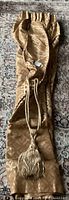 One long drapery panel folded with attached gold tassel visible, showing fabric color and texture.